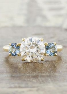 an engagement ring with three stones on the side and one stone in the middle, sitting on top of a wooden surface