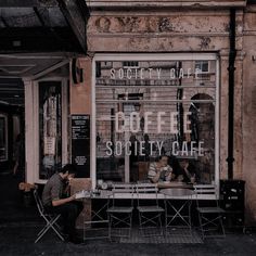 two people sitting at a table in front of a cafe