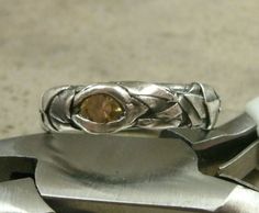 a silver ring with a brown stone in it sitting on top of some metal tools