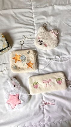 three purses are laying on a bed with white sheets and teddy bear keychains