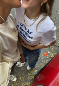 two young women are kissing each other on the street while one woman is wearing a white t - shirt