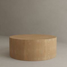 a round wooden table sitting on top of a white floor next to a gray wall