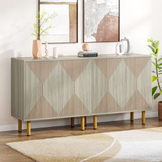 a sideboard with two vases on top of it next to a rug and potted plant