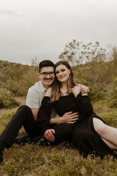 a man and woman are sitting in the grass together, posing for a photo with their arms around each other