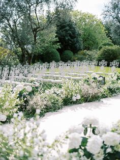 an outdoor ceremony with white chairs and flowers in the foreground, surrounded by trees