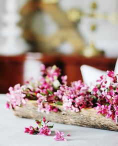 small pink flowers are placed in a wooden basket on a table with white linens