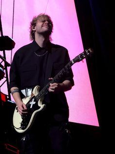 a man standing in front of a pink screen holding a guitar and looking up at the sky