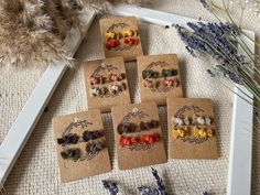 six pairs of earrings are on the table next to some dried flowers and lavenders