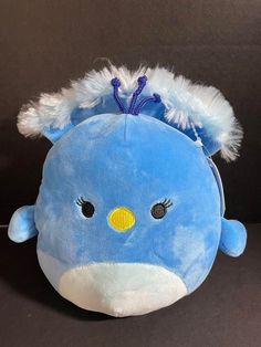 a blue stuffed animal with white feathers on it's head and eyes, sitting against a black background