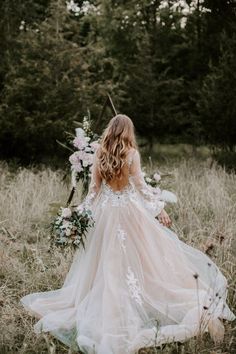 a woman in a wedding dress walking through tall grass with her back to the camera