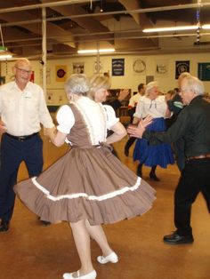 an older couple dancing in a large room with other people standing around and looking on