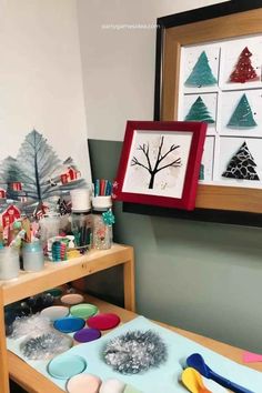 a wooden table topped with lots of crafting supplies next to a framed christmas tree