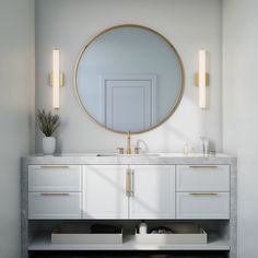 a bathroom vanity with a round mirror above it and two candles on the counter top