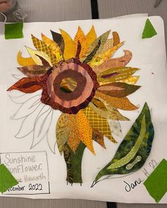 a sunflower made out of scrap paper on a piece of white paper with green and yellow strips