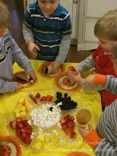 three young boys are eating fruit and crackers on a yellow tablecloth in the kitchen