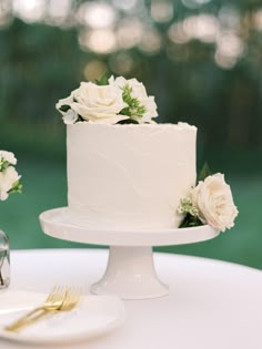 a white wedding cake with flowers on top sitting on a table next to a knife and fork