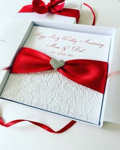 a wedding card with a red bow and diamond heart in the middle, on top of a white envelope