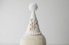 Adorable little  party hat for every occasion. The base of the cone is made of card stock and the top is made of a linen fabric in off white color, just as pictured.  The front embellishment is hand embroidered with love and attention to detail.  This hat can be customized if you order at least 2.5 weeks before the day it needs to arrive, please contact me to confirm if I can make to your specifications. MEASUREMENT This hat fits all sizes and ages. The hat including the pompom measures about 6 inches tall and 3 inches in diameter.  SHIPPING INFO This item is made to order and will ship in 1-7 business days, sooner if it is in stock If you need an item at an specific time, please contact me and I will do my best to accommodate. If an RTS item is ordered with a made-to-order item, the order Whimsical White Mini Hat For Gifts, Whimsical White Mini Hat As Gift, White Hat For First Birthday In Spring, White Hats For First Birthday In Spring, White Hats For First Birthday And Spring, Whimsical White Hat For Birthday, Whimsical White Mini Hat For Garden Party, White Handmade Hats For Birthday, Cone Flowers