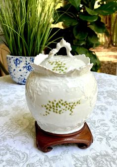 a white vase sitting on top of a wooden stand next to some potted plants