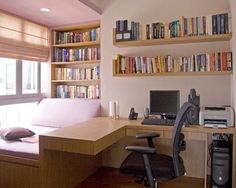 a computer desk sitting under a window next to a bookshelf filled with books