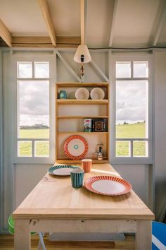 a table with plates and cups on it in front of two large windows that look out onto an open field