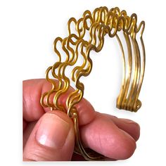 a hand holding a gold colored metal object with wavy lines on it's side