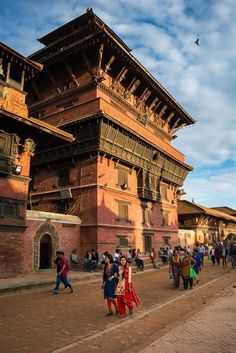 people are walking around in front of an old building with wooden carvings on the roof