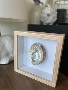 a seashell in a wooden frame on a table next to a lamp and figurine