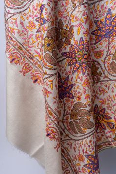 The Hand-Embroidered Sozni Garden Tapestry Pashmina Shawl is an opulent ode to the intricate gardens of the East. Artisans have hand-stitched a riot of floral majesty, with each petal and leaf crafted in vibrant saffron, amethyst, and ruby threads, across the shawl’s luxuriously soft cream pashmina. This shawl serves not merely as a garment but as a conversation with history, with every thread woven into a story of traditional Kashmiri splendor. It’s a garment destined for the wardrobes of those Bohemian Beige Pashmina Shawl, White Bohemian Pashmina Shawl For Festive Occasions, Cream Bohemian Pashmina Shawl For Wedding, Festive White Bohemian Pashmina Shawl, Festive Bohemian White Pashmina Shawl, White Pashmina Shawl For Festivals, Festive Cream Pashmina Shawl, White Bohemian Pashmina Shawl With Motifs, Cream Bohemian Shawl With Intricate Embroidery