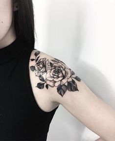 a woman's arm with flowers and leaves tattooed on her shoulder, in front of a white wall