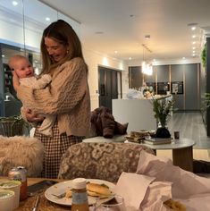 a woman holding a baby in her arms while standing next to a table with food on it