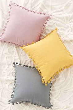 three pillows with pom poms on top of a white bedding sheet,