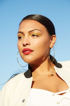 a woman wearing large gold hoop earrings and a white shirt is looking at the camera