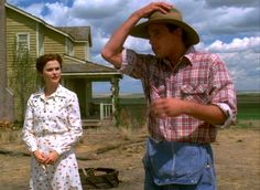 a man and woman standing in front of a house with a hat on their head