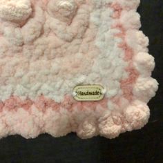 a pink and white teddy bear laying on top of a black surface with a name tag