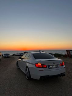 a white car parked on the side of a road next to the ocean at sunset