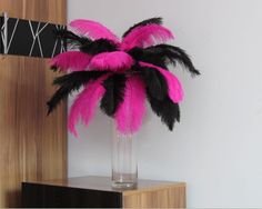 a vase filled with pink and black feathers on top of a wooden table next to a white wall