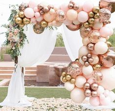 a wedding arch decorated with pink and gold balloons, greenery and white draping