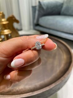 a woman's hand holding a diamond ring on top of a table in front of a couch