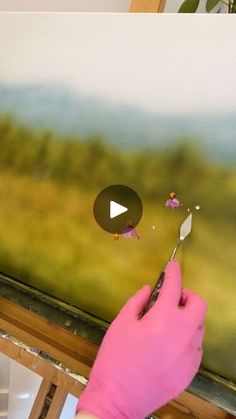 a person in pink gloves painting a landscape