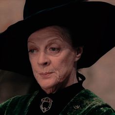 an older woman wearing a black hat and green velvet coat, looking at the camera