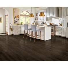 a large kitchen with wooden floors and white cabinets, along with two bar stools