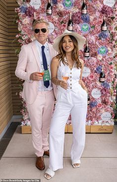 two people standing next to each other in front of a wall with flowers on it