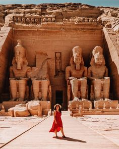 a woman in a red dress standing in front of an ancient building with statues on it