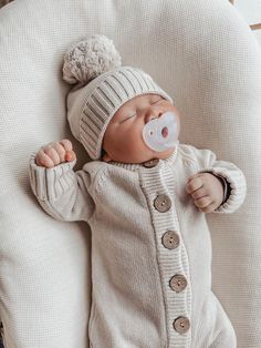 a baby wearing a white sweater and hat with a pacifier in it's mouth