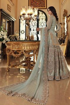 a woman standing in front of a table wearing a long dress with an intricate design