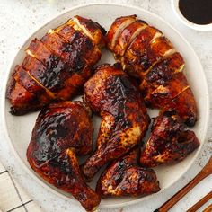 a white plate topped with sliced chicken next to chopsticks and sauce on top of a table