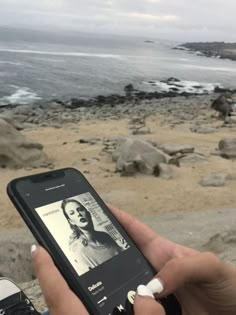 someone holding up their cell phone to take a picture of the beach with her face on it