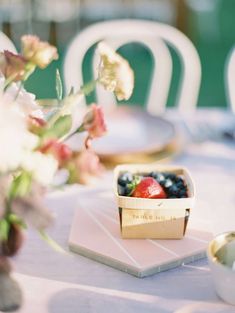 there is a small bowl of fruit on top of a table with flowers in the background