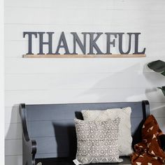 a bench with pillows and a sign that says, thankful on the wall above it